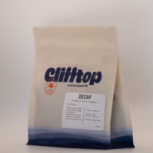 Load image into Gallery viewer, A bag of Clifftop Coffee Roasters Decaf coffee on a light gray background. The bag is off-white with a blue and navy gradient at the bottom and features the Clifftop logo in dark blue with an orange sun graphic.